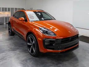 Orange Porsche SUV parked in a modern showroom with polished concrete floor and white walls.