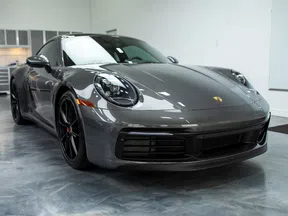 Sleek gray Porsche 911 sports car parked indoors on polished concrete floor with black wheels and modern headlights.