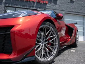 Close-up of a red sports car wheel and sleek body design parked outside a building with garage doors.