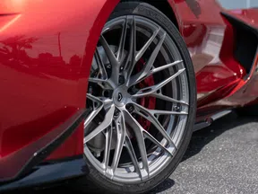 Close-up of sleek silver alloy wheel on red sports car with detailed tire and brake components.