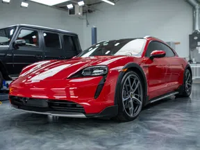 Red Porsche Taycan electric sports car parked indoors beside a black SUV on polished floor.
