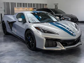 Silver sports car with blue racing stripe parked in a polished showroom with another black car in background