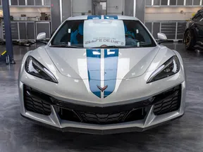 Front view of a silver Chevrolet Corvette with blue racing stripes in a workshop.