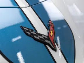 Close-up of Chevrolet Corvette emblem with cross flags on blue and white car hood.