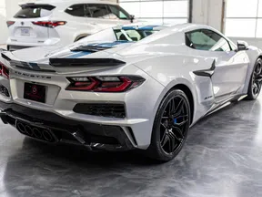 White Chevrolet Corvette sports car rear and side view in a showroom with polished floor and nearby white SUV.