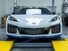 Front view of a white Chevrolet Corvette sports car inside a garage with a lift and yellow ramps.