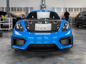 Front view of a blue sports car with black hood in a modern automotive workshop.