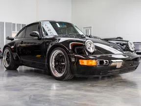 Black vintage Porsche sports car with wide body kit parked indoors on polished concrete floor.