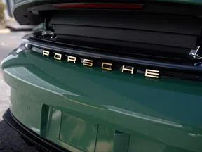 Close-up of green Porsche car rear with gold logo and open trunk showcasing sleek design elements.
