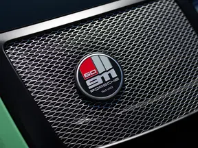 Close-up of Porsche 911 60th anniversary badge on a honeycomb car grille with green paint edges.