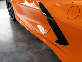 Close-up of an orange sports car side with black air vent and sleek smooth paint finish.