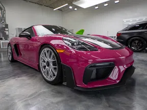 Sleek magenta sports car with silver rims parked inside a glossy showroom with other vehicles.
