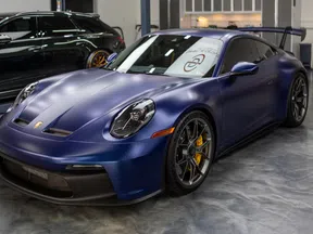 Matte blue Porsche sports car with yellow brake calipers parked indoors on polished concrete floor.