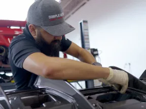 Mechanic wearing gloves and a cap working on the engine of a car in a garage with tools in the background