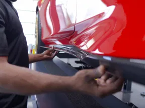 Mechanic installing or inspecting a black side skirt on a polished red sports car in a garage.