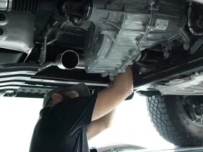 Mechanic inspecting and repairing the underside of a vehicle in a workshop with raised car and tools nearby