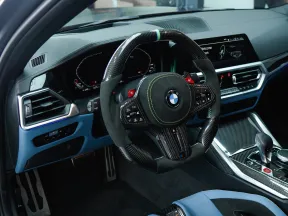 BMW car interior featuring carbon fiber steering wheel, digital dashboard, and blue leather seats.