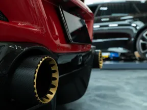 Close-up of a red sports car's rear exhaust with gold trim, blurred luxury cars in background inside showroom.