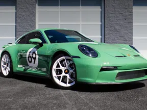 Green Porsche 911 sports car with white racing number 69 parked in front of a building garage door.