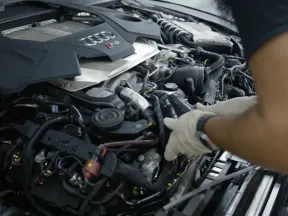Mechanic wearing gloves repairing a detailed Audi RS engine under the hood of a car.
