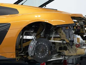 Yellow sports car with rear panels removed showing detailed suspension and brake system in workshop setting