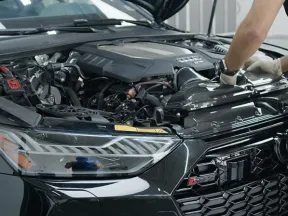 Mechanic wearing gloves repairing a black car engine under an open hood in a garage