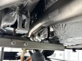 Close-up of a car's undercarriage showing shiny stainless steel exhaust pipes and mounting brackets