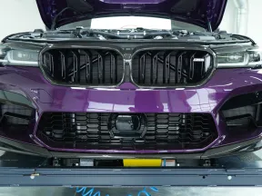 Front view of a purple car with open hood showing grille and headlights in a garage setting