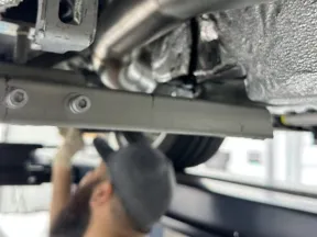 Mechanic inspecting car suspension components under vehicle on a lift in a garage.