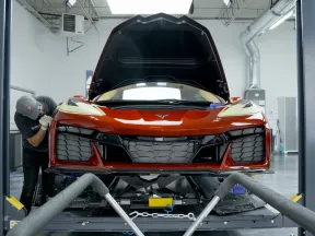 Front view of a red sports car with open hood in a workshop being inspected by a technician.