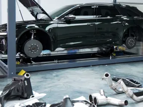 Black car lifted on a hydraulic lift in a garage with removed wheels and exhaust parts on the floor