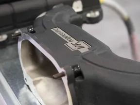 Close-up of a car engine intake manifold with a black finish and a logo on a metallic surface.