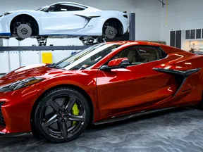 Red sports car parked in a garage with a white sports car lifted in the background, showcasing sleek design.