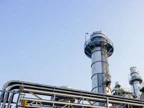 Industrial refinery towers and piping against a clear blue sky at an energy plant.