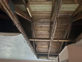 Ceiling with exposed wooden beams and damaged ceiling drywall in a residential room with light pink walls.