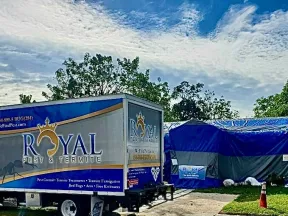 Royal Pest & Termite service truck parked near a blue tent with trees and cloudy sky in the background.