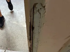 Worn and damaged door frame with cracked paint and dirty tiled floor with footprints near an entrance.