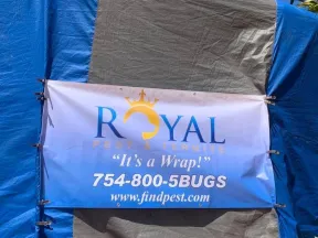 Royal Pest & Termite banner on a wrapped structure with phone number and website under clear blue sky.