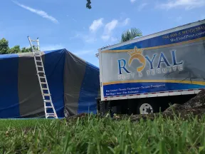 Royal Pest & Termite truck next to a tented house with ladder for termite fumigation service under blue sky.