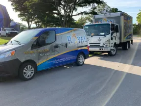 Royal Pest Termite service vehicles parked on a sunlit road next to trees during daytime.
