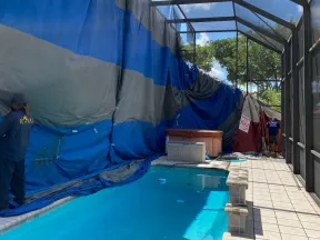 Indoor pool with blue water under a metal frame enclosure and large blue tarps covering one side during maintenance.
