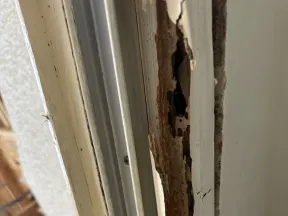Close-up of severely damaged and rotting wooden door frame with peeling paint and exposed wood interior.