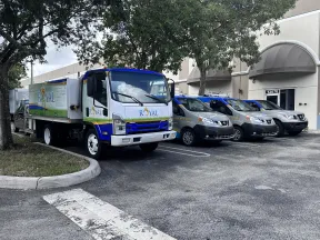 Royal Landscape Maintenance truck and company vans parked outside an office building under trees on a sunny day