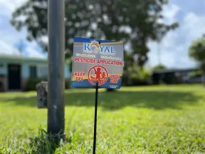 Royal Pest & Termite sign warns of pesticide application with instructions to keep off until dry on green lawn.