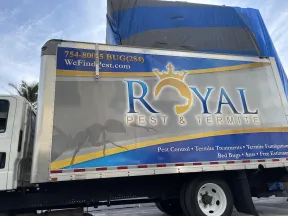 Side of a Royal Pest & Termite truck with logo, contact info, and pest control services listed under a blue sky.