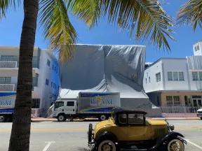 Vintage yellow car parked on a sunny street with palm trees and a covered building in the background.