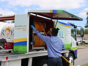 Pest control worker in blue shirt handling hose from Royal Pest & Termite truck on street under blue sky.