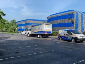Royal Pest Control trucks parked near large buildings covered with blue and gray protective tarps under a clear sky