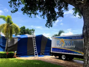 Royal Pest & Termite truck parked beside a house covered with a large blue and black tarp for fumigation under a sunny sky.