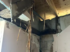 Interior corner of room with severe ceiling damage and exposed wooden beams and plaster hanging down.